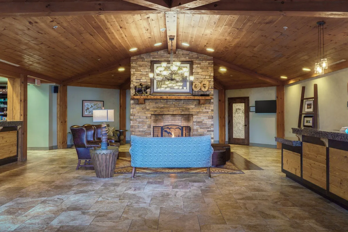 A warm, inviting living area featuring a stone fireplace, a plush blue couch, exposed wooden beams, and a cozy atmosphere ideal for relaxation or social gatherings. The space radiates comfort, making it perfect for group movie nights, sharing stories, or simply unwinding by the fire.