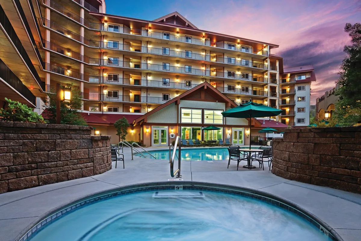 An exterior view of a shared amenities area shows a sparkling swimming pool and jacuzzi surrounded by lounge chairs, with the building facade in the background. The space is designed for outdoor dining, socializing, and enjoying the mountain air, especially during sunset or family reunions.