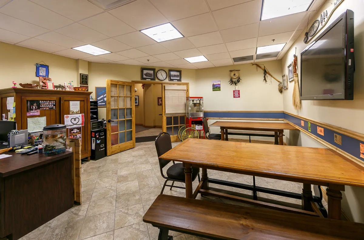 A casual interior space with wooden tables, a reception desk, and a TV on the wall, offering a welcoming spot for socializing, informal gatherings, or family meals.